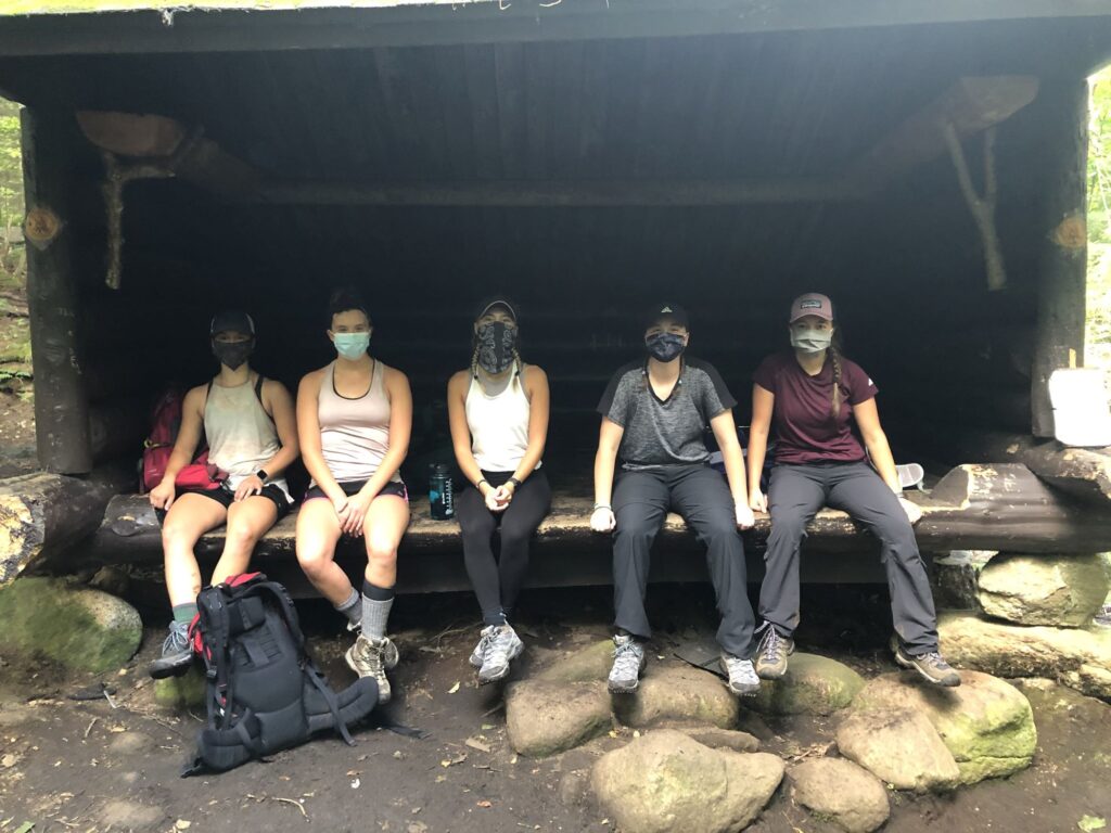 Female students wearing masks sitting on a wooden lean-to.