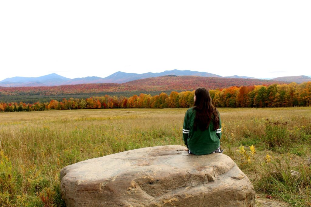 A young woman sitting on a rock looking out at the mountains.